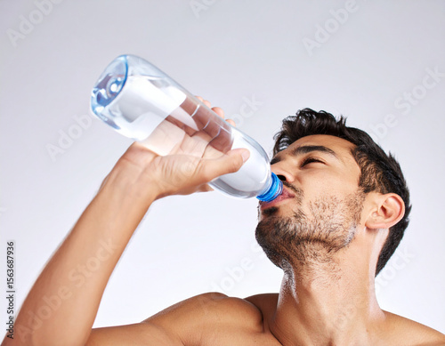 Un hombre joven bebiendo de una botella de agua para la sed e hidratarse durante una ola de calor con altas temperaturas en verano con fondo blanco
