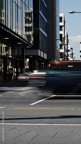 Urban street scene capturing blurred movement of pedestrian walking alongside fast moving vehicles, conveying city's dynamic energy against architectural backdrop