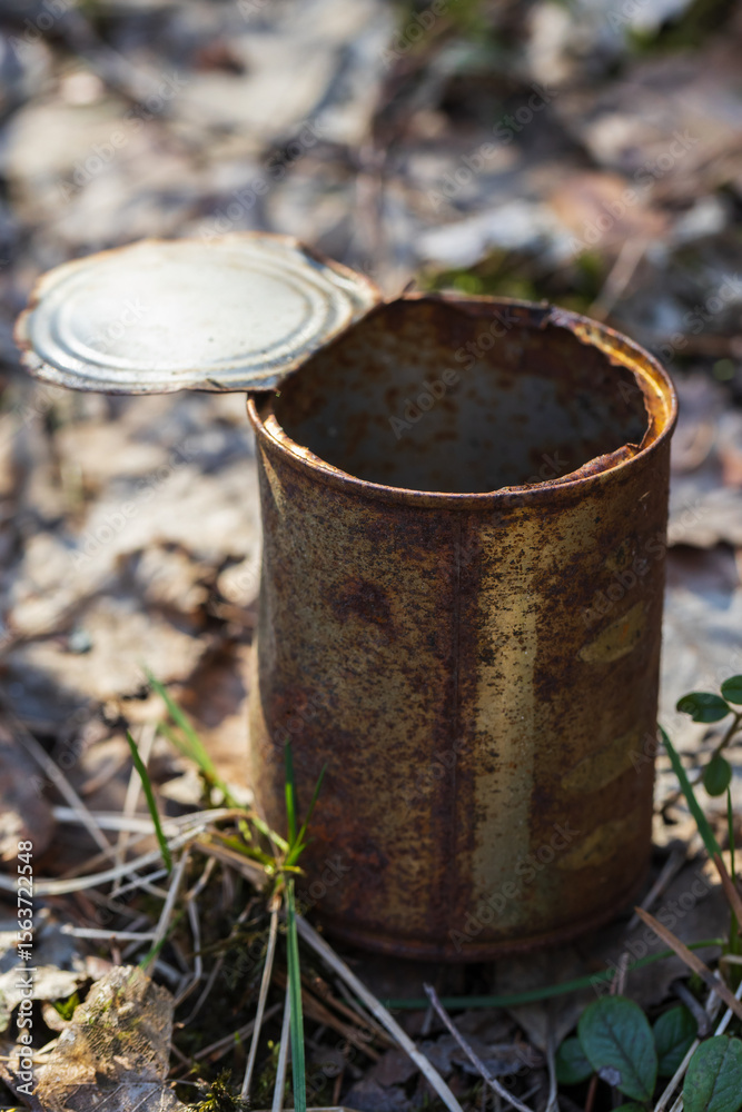 Naklejka premium A rust-covered metallic can is abandoned on the ground surrounded by leaves