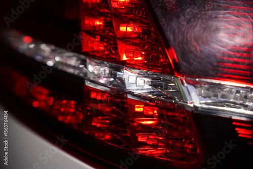 Close-up of modern red and white LED car tail light with geometric internal structure. Macro shot of vehicle lighting system. Automotive detail and safety equipment concept. 