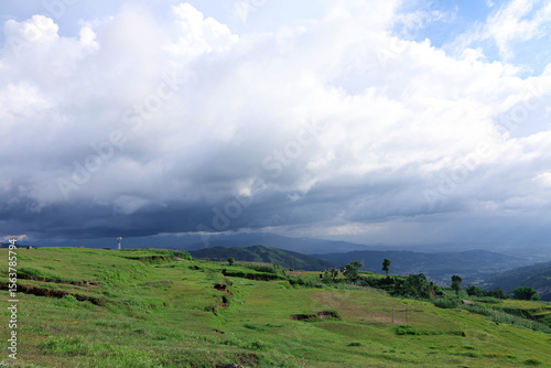 A dramatic sky unfolds over the lush green hills of Nepal, where light and shadow dance on the rolling landscape. Nature’s quiet masterpiece.