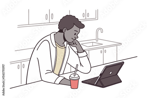 Young man in a lab coat thoughtfully observing a tablet device while enjoying a drink in a modern kitchen setting