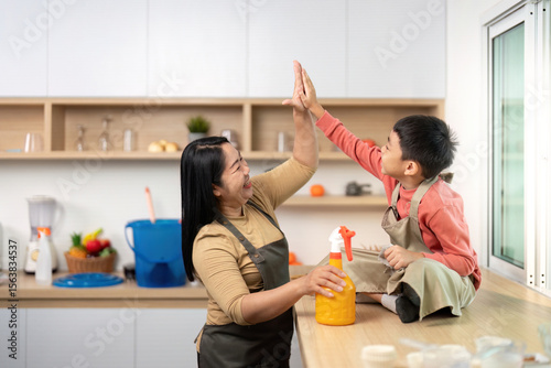 Family Bonding During Cleaning. Mother and son share a high-five while tidying up the kitchen.
