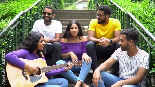 Indian asian university student singing song with guitar in college campus and friends enjoying