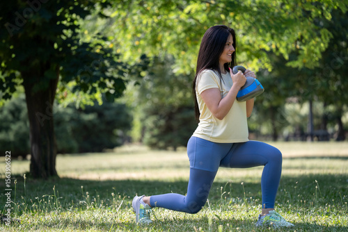 Beautiful smiling woman doing kettlebell lunge  workout in the park in the morning, active and healthy lifestyle


