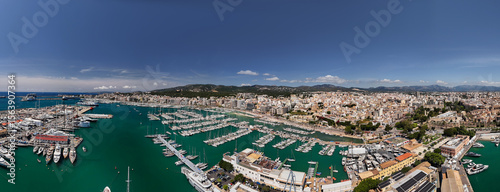 An aerial view of Palma de Mallorca's vibrant marina filled with boats, set against the backdrop of the grand cathedral and a sprawling coastal city under a blue sky
