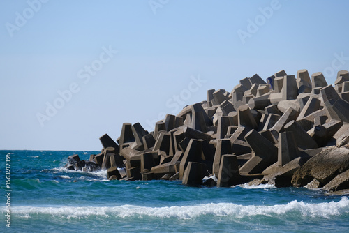 Fototapeta Naklejka Na Ścianę i Meble -  Concrete wave breaker tetrapods protecting the shoreline from strong sea waves under a clear blue sky.