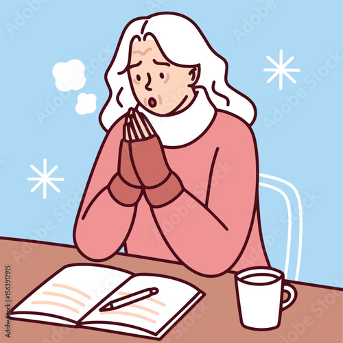 Elderly woman studies or reads in unheated room, warming hands on hot mug to stay warm during winter cold
