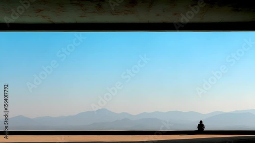 Person seated, looking at a mountain range, blue sky vista