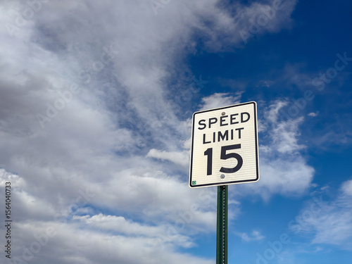 Speed limit sign for 15mph isolated against a blue sky with white clouds. No people. Copy space.