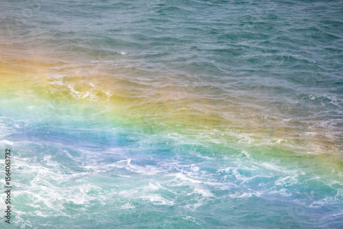 Fototapeta Naklejka Na Ścianę i Meble -  Rainbow against the backdrop of waves crashing on the shore