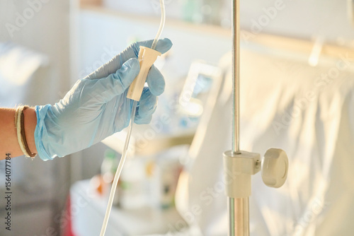 Nurse’s gloved hand adjusts the intravenous flow valve delivering medication through an infusion tube to a patient