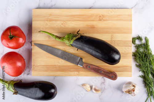 Top view of eggplant with knife on wooden cutting board.