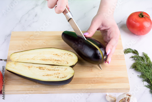 Cutting eggplant into two halves with a knife.