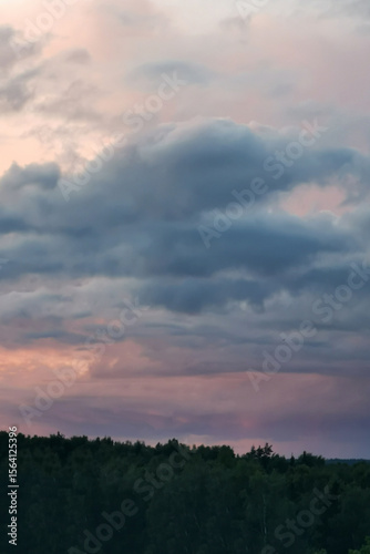 Dramatic clouds in a twilight sky, showcasing shades of gray and pink, hovering over a lush green forest, creating a serene and tranquil atmosphere in nature