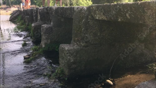 Medieval stone bridge with people walking on it, river beach in northern Portugal, Europe