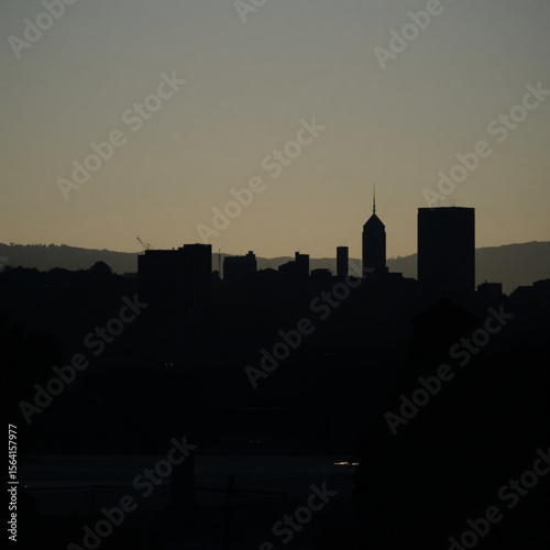 Silhouette of a city skyline at dusk with hills in the background and a light colored sky above it all