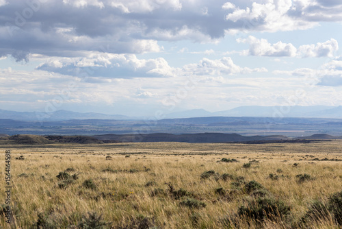 Scenic vista showing grassy prairie with layers of mountains and hills in the distance under a stormy sky with dark  nimbostratus nimbus rain clouds creating haze far away