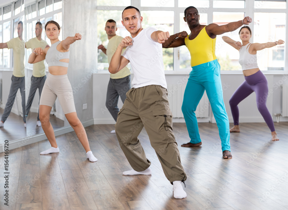 Naklejka premium Sporty smiling young Asian guy practicing rhythmic aerobics during group workout in spacious mirrored fitness studio. Active lifestyle concept..