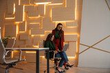 Two businesswomen working in a modern office, one sitting with a laptop, the other standing and discussing, stylish teamwork and collaboration concept with warm lighting.