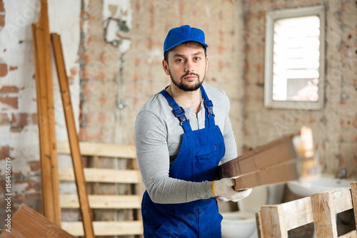 Professional builder working on a construction site indoors holds wooden bars in his hands photo