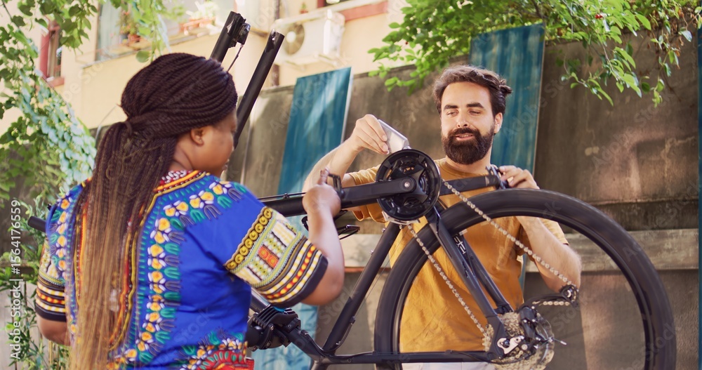 Obraz premium African american girlfriend assisting caucasian boyfriend with lubricating rusty bicycle chain outside as summer maintenance. Sporty multiethnic couple greasing bike chain in yard for safe cycling.