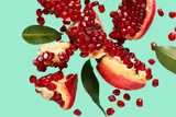 Flying fresh pomegranates with seeds and leaves on turquoise background