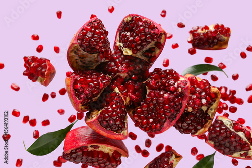 Flying fresh pomegranates with seeds on lilac background