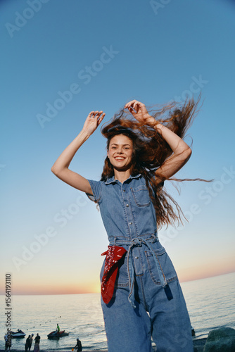 lifestyle woman in modern boho-western denim outfit enjoys carefree moment by the sea with natural light and film color effect at sunset