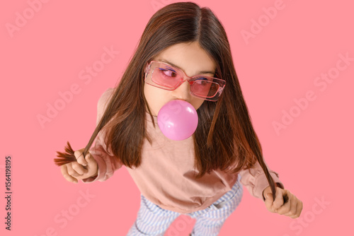 Trendy girl blowing bubble gum on pink background