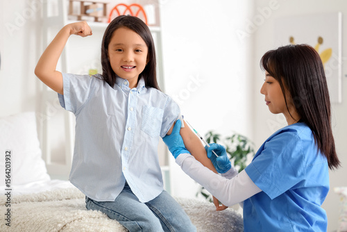 Happy little Asian girl receiving vaccine at hospital