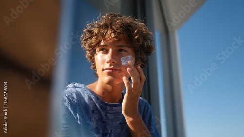 Sunscreen Application: A young man gently applies sunscreen to his face, protecting his skin against the sun's rays with a touch of care and mindful health, basking in daylight.