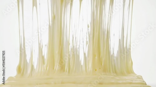 Close up of a thick, dripping, yellow substance with air bubbles against a white background studio shot