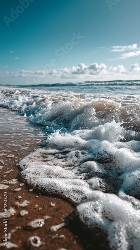 Waves gently crashing on sandy beach under clear blue sky on sunny day