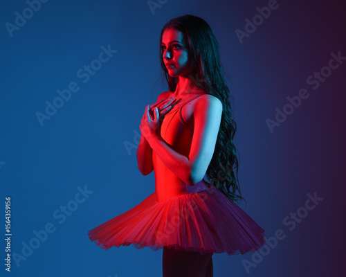 Dramatic 3/4 portrait of ballerina in red tutu and pointe shoes under moody blue and red neon lighting, expressive theatrical pose in artistic studio with cinematic contrast and vivid colour