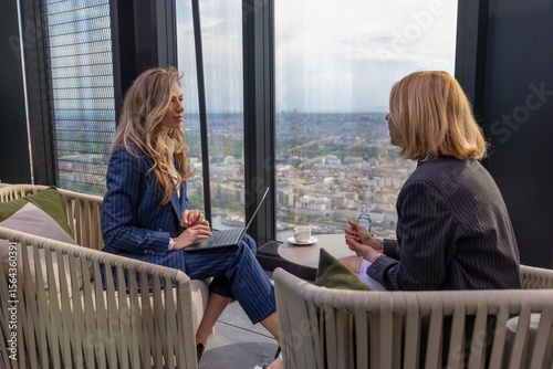 In a sleek, contemporary office atmosphere, two professional women are deeply engaged in a meaningful conversation while enjoying an impressive view of the vibrant city skyline outside their window