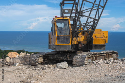 an old crawler crane with a lattice boom, standing on a construction site near a cliff by the sea