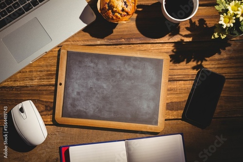 Wooden-framed chalkboard is being shown in flat design workspace with laptop, coffee cup, flowers