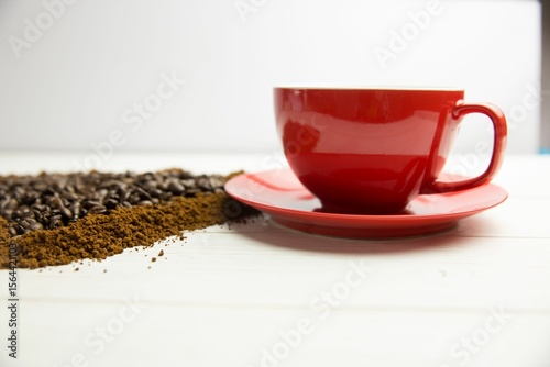 Showing flat-lay red coffee cup resting on wood plank, spilling roasted beans and coffee grounds