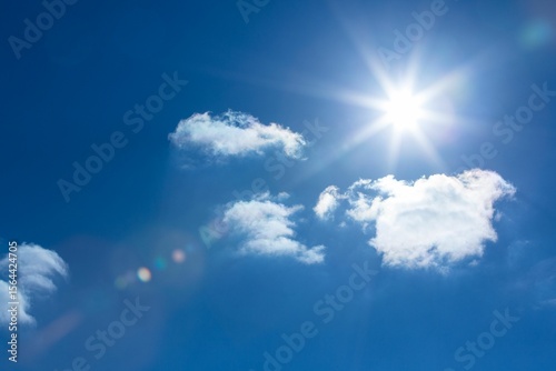 Sun is shining in flat design deep blue sky, with fluffy clouds and vibrant lens flare