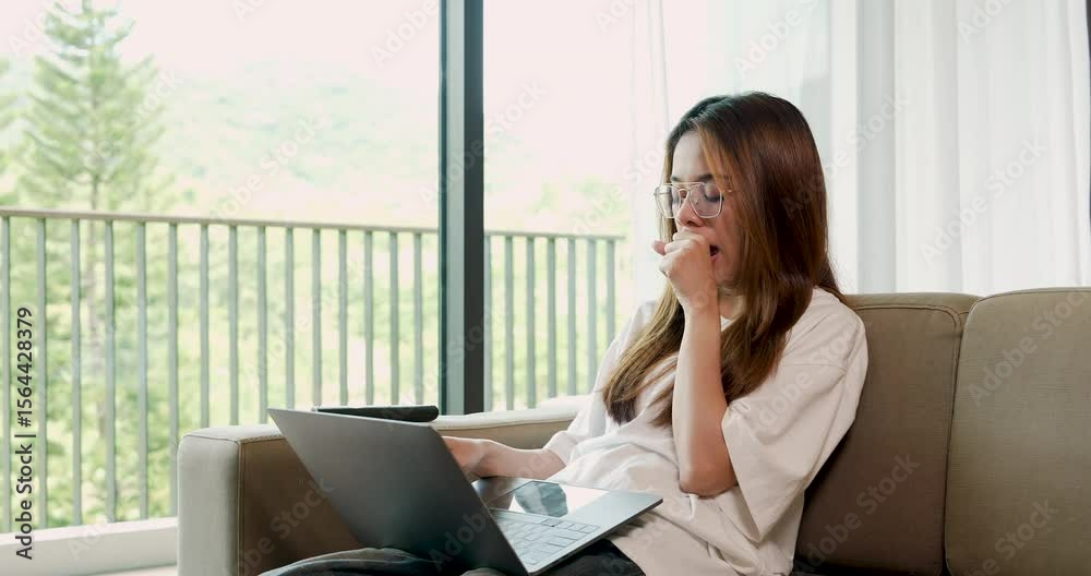 Asian adult woman yawns and rubs eyes while sitting on sofa with laptop, experiencing sleepiness and mental exhaustion during long remote work routine inside home environment Asian adult woman yawns and rubs eyes while sitting on sofa with laptop, experiencing sleepiness and mental exhaustion during long remote work routine inside home environment