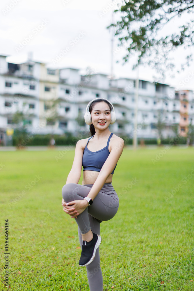 Fototapeta premium Portrait of a smiling young fitness asian girl doing stretching in the park.Healthy women exercise concept. 