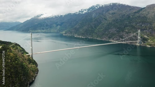 Wallpaper Mural Hardanger Bridge gracefully traverses fjord surrounded by mountains with snowy caps. Long slender bridge creates striking line over natural landscape Torontodigital.ca