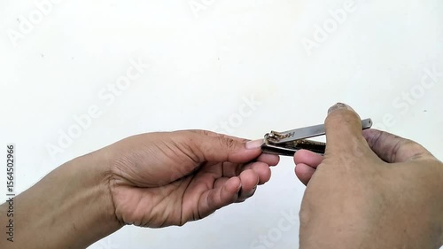 Close-up of a man’s hands using a metal nail clipper to trim fingernails. The plain white background emphasizes the personal grooming action.