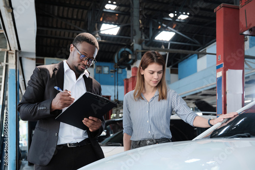 Warranty service business, White female client inspections sign declarations and contract from Black male insurance agent, accept car accident claims, fix and maintain at automotive garage station.