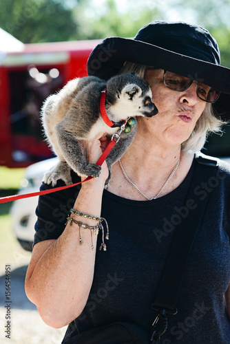 Woman puckers lips as lemur sits on her shoulder outdoors.