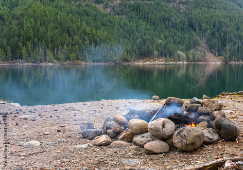 Campfire by the lake surrounded by forest on a calm day