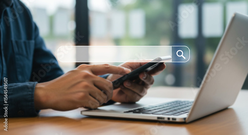 Web Search Interaction: A person, with focus, utilizes a smartphone alongside a laptop computer to search the World Wide Web, as if in their own personal office.