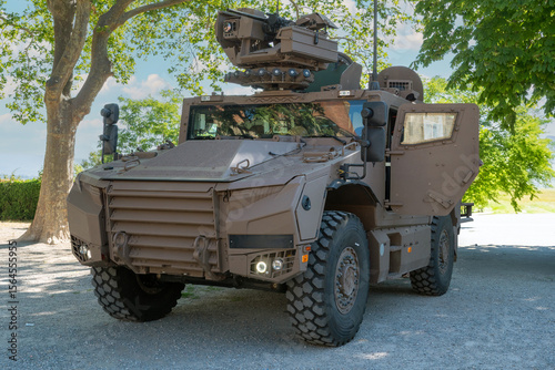 French military vehicle with a gun on top. The vehicle is brown. It is parked in a parking lot