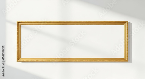 A golden rectangular picture frame hangs on a white wall, casting shadows.
